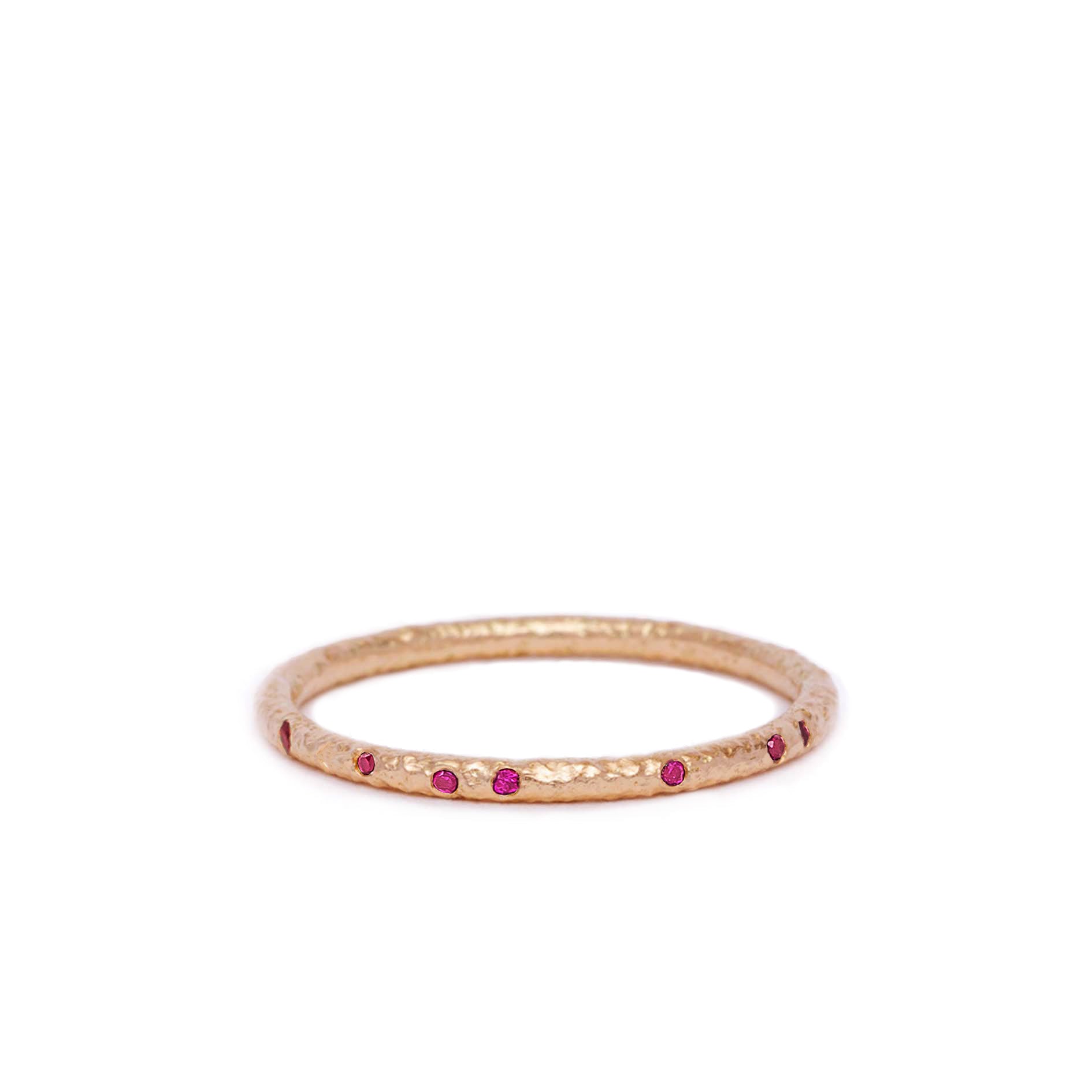 Rose gold ring with embedded red ruby gemstones on a white background