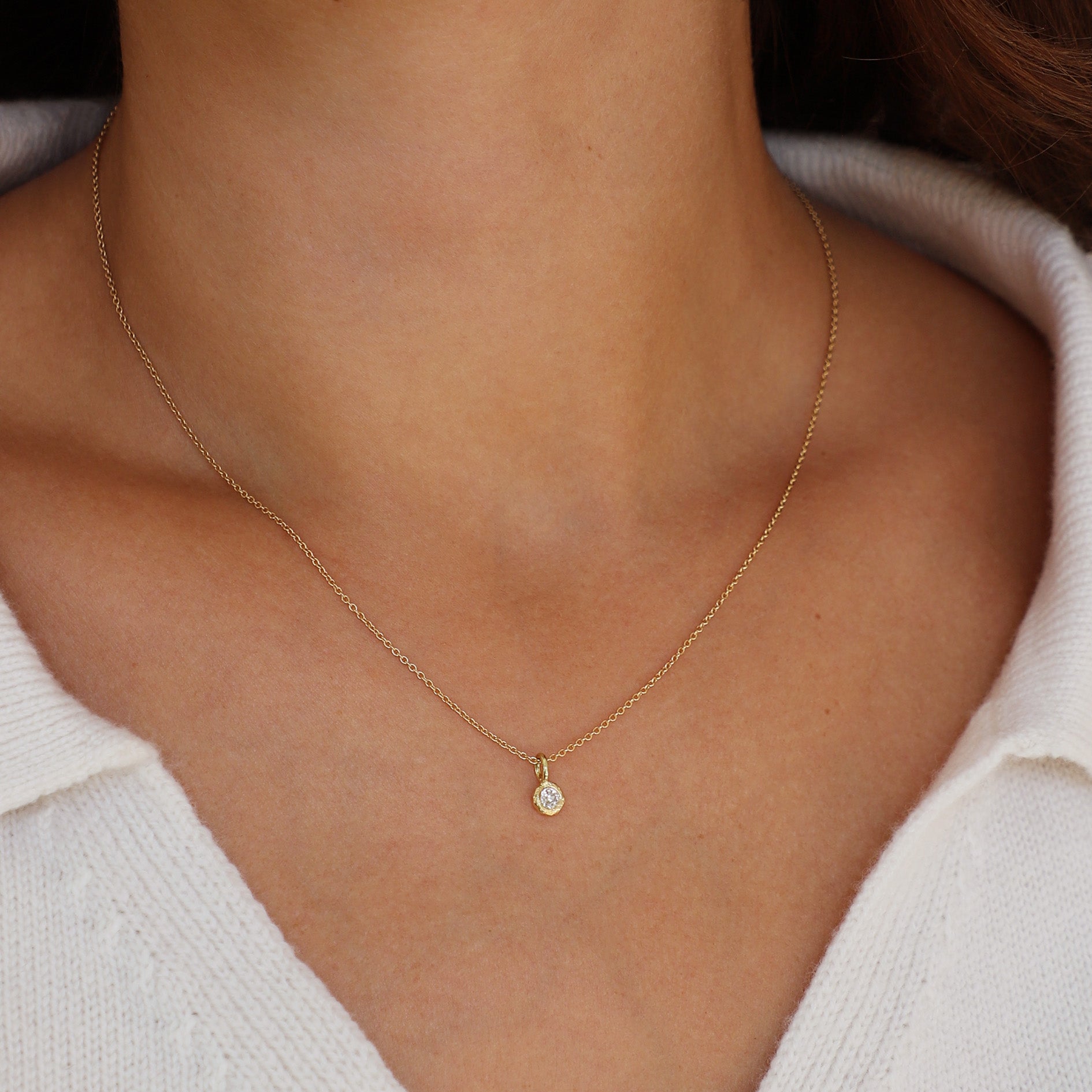 Gold and diamond necklace on a person wearing a white sweater.