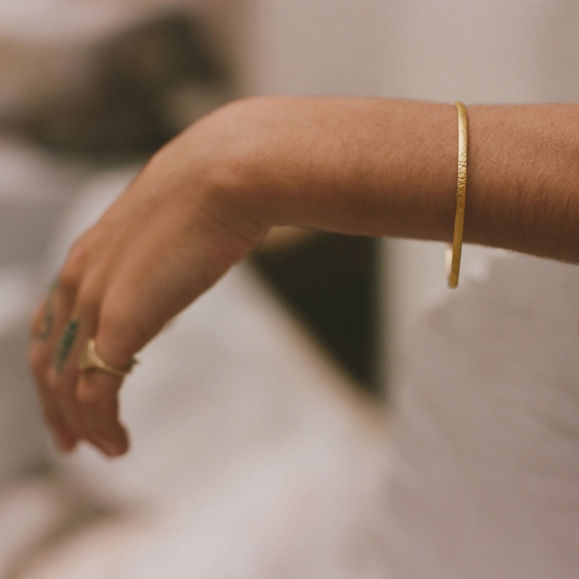 Close-up of a person's arm with gold bracelets on a blurred background
