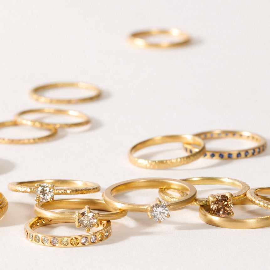 maya selway fine jewellery still life, scattering of many matte and textured 18ct yellow gold and diamond rings